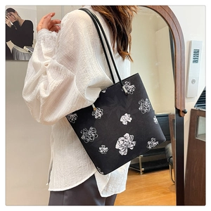 Detail of black tote bag with white floral print shown as a shoulder bag on a model