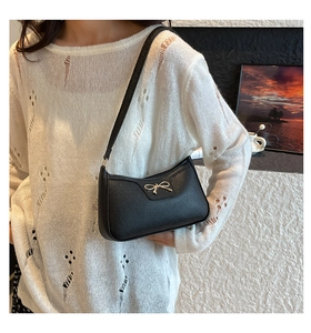 Detail of black pebbled leather baguette bag featuring a silver bow and shoulder strap