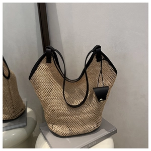 Detailed macro view of woven beige tote bag featuring black leather trim and shoulder straps