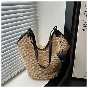 Detail of hollow woven straw tote bag with black leather straps on a sunny windowsill