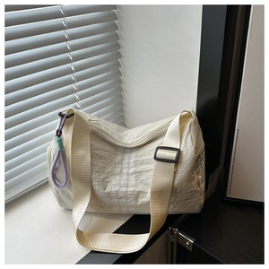 Close-up of beige oxford shoulder bag with striped details and a braided colorful charm