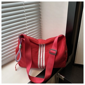 Close-up of red nylon cylinder crossbody bag featuring white stripes and creative pendant