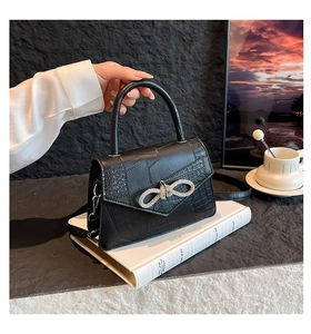 Detail of black crocodile texture handbag with rhinestone bow buckle and leather strap
