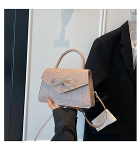 Detail of pink faux crocodile handbag featuring a sparkling rhinestone bow and top handle