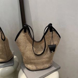 Handwoven straw tote bag with black leather trim and decorative pendant for beach holidays
