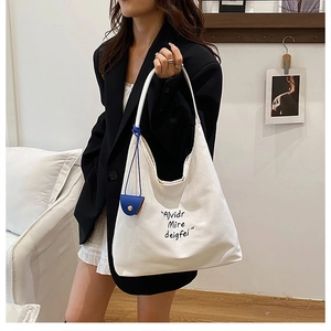 Detailed close-up of large canvas tote bag with blue pendant and black typography print