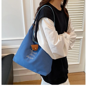 Detail of blue canvas tote bag with white embroidery and brown leather trim on model