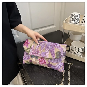 Detailed view of floral sequin embroidery and gold chain on a straw envelope bag