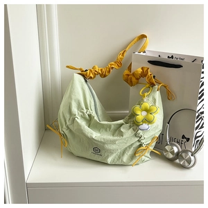 Detail of light green pleated shoulder bag with yellow strap and flower charm
