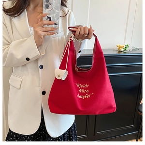 Detail of red canvas tote bag featuring white letter embroidery and a side hanging pouch