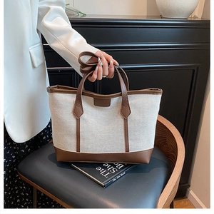 Detail of canvas tote bag with brown leather trim and adjustable shoulder strap on chair