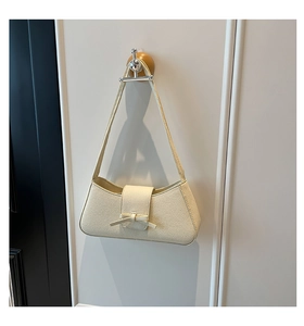 Detalle del bolso baguette blanco crema con lazo decorativo y textura de cuero lichi