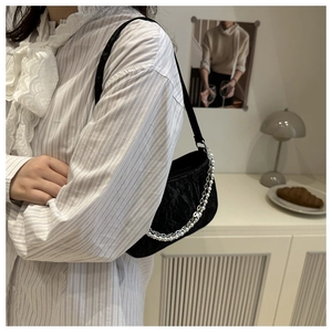 Detail of black pleated underarm bag with elegant pearl and silver metal double chains