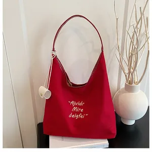 Detail of red canvas tote bag featuring white embroidery and elegant lifestyle props