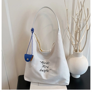 Detail of white canvas tote bag featuring stylish black lettering and blue circular pouch charm