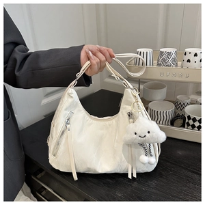 Detail of a creamy beige nylon crescent shoulder bag with silver zippers and plush charm