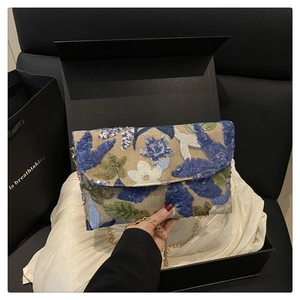 Detailed close-up of sequin floral embroidery on a straw envelope clutch with gold chain