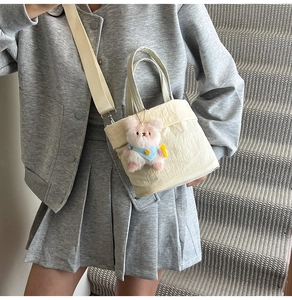 Detail der cremefarbenen Canvas-Beuteltasche mit rosa Plüschbär-Anhänger und Tragegurt