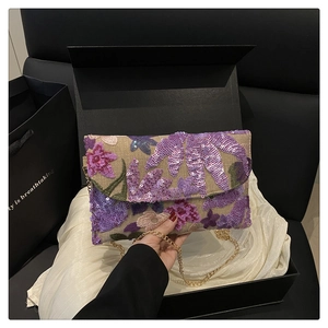 Macro view of sequin floral embroidery and gold chain strap on a straw clutch bag