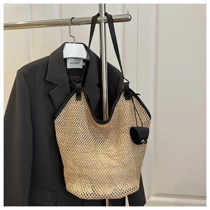 Détail du sac cabas en paille tressée avec anses en cuir noir et pendentif décoratif