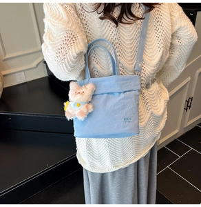 Détail du sac bandoulière bleu clair avec breloque d'ours en peluche et logo de marque