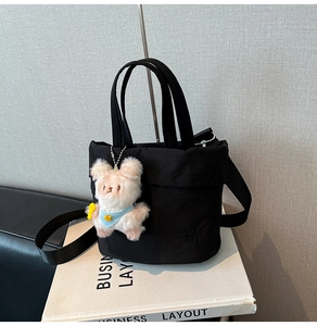 Detail der schwarzen Nylontasche mit geprägtem Logo, Gurt und Plüschbär-Anhänger