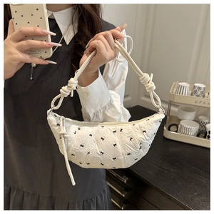 Close-up of white crescent bag featuring black bow embroidery and knotted shoulder strap