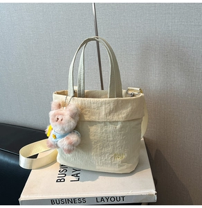 Detail der cremefarbenen Nylon-Beuteltasche mit Bärenanhänger und Bestickung