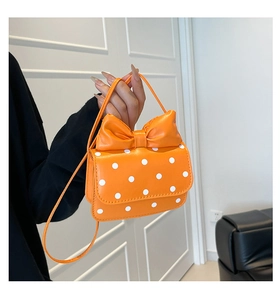 Detail of orange crossbody bag with white polka dots and a large decorative bow
