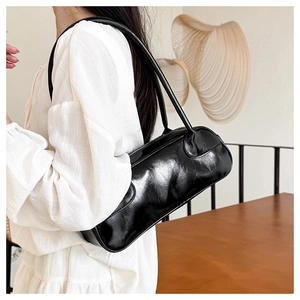 Close-up of a glossy black baguette bag with long straps worn on the shoulder in a room
