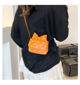 Detail of vibrant orange polka dot crossbody bag with large bow worn by a model