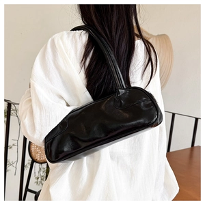 Detail of black glossy baguette bag with wrinkled leather texture on a female shoulder