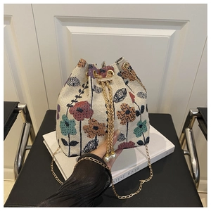 Detail of woven bucket bag with floral patterns, gold chain, and pearl drawstring accents