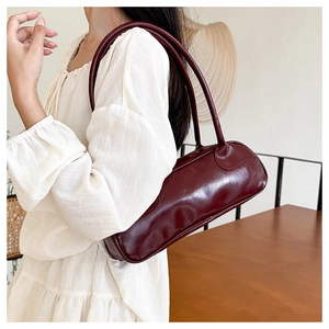 Detail of a deep red glossy cylindrical baguette bag with sleek twin shoulder straps