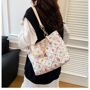 Detail of cream tote bag with cartoon patterns, gold chain strap and plush rabbit charm