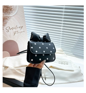 Detail of a mini black polka dot crossbody bag featuring a large decorative 3D bow on top