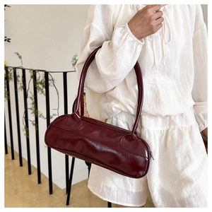 Detail of burgundy cylinder bag worn over shoulder on a white casual outfit