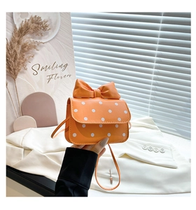 Detail of a bright orange mini crossbody bag with white polka dots and a large bow