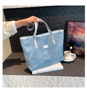 Primo piano di una borsa tote lavata azzurra con manici argentati posata su un libro
