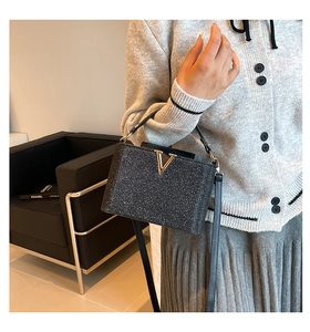 Détail du sac à main noir scintillant avec boucle dorée en V et poignée en cuir