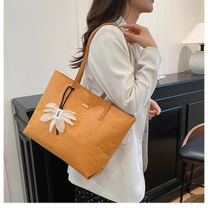 Détail du sac cabas orange avec texture cuir et pendentif floral sur le mannequin