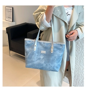Dettaglio della borsa tote azzurra con trama marmorea, rivetti dorati e logo moda in metallo