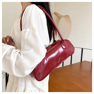 Detail of burgundy baguette bowling bag worn as an underarm shoulder bag for women