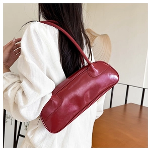 Glossy burgundy leather baguette bag worn by a model in a minimalist indoor setting