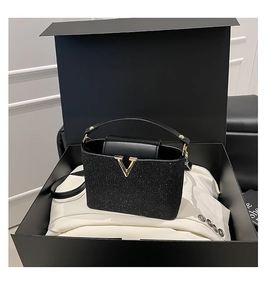 Gros plan d'un sac à main noir pailleté avec boucle dorée en V dans un coffret cadeau