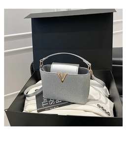 Détail du sac seau à paillettes argentées avec logo V doré dans une boîte cadeau