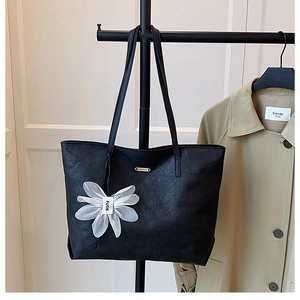 Détail du sac cabas plissé noir avec plaque dorée et pendentif fleur blanche soyeux