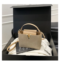 Détail du sac à main pailleté doré avec ornement en V métallique sur boîte cadeau