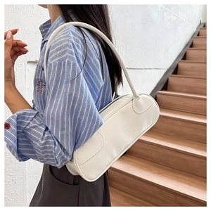 Minimalist white cylindrical baguette bag with high gloss finish worn as an underarm bag