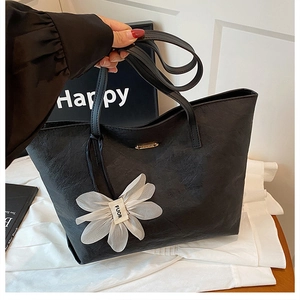 Détail du sac cabas en cuir noir avec logo doré et pendentif fleur en résille blanche